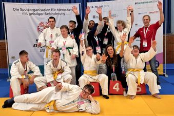Judoteam von Menschen mit Behinderung jubelt nach Wettkampf gemeinsam auf der Matte.