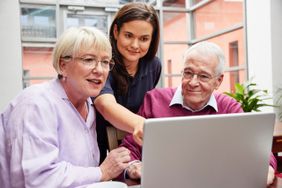zwei Seniorinnen und eine Kursleiterin blicken auf einen Computerbildschirm. 