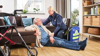 Mitarbeiterin der Malteser hilft einem Mann beim Aufstehen