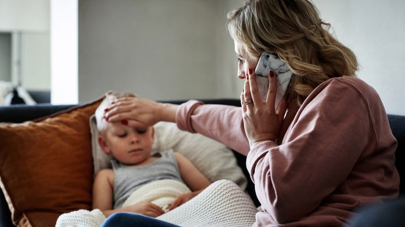 Eine Mutter am Telefon mit der Hand auf der Stirn eines Jungen.
