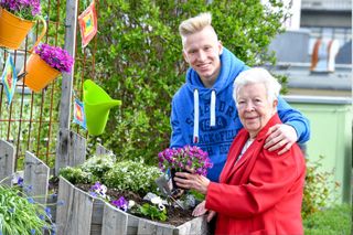 Begleiter des sozialen Dienstes pflanzt mit Bewohnerin Blumen ein