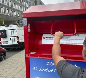 Ein Mann schiebt die Klappe eines Malteser Altkleidercontainers auf. Rund 7.700 Container dieser Art stehen in Deutschland. (Foto: Richardt/Malteser)