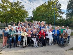 Viele Seniorinnen und Senioren haben sich für ein Gruppenbild im Freien zusammengefunden. In der ersten Reihe sind bewegeungseingeschränkte ältere Menschen im Rollstuhl positioniert.
