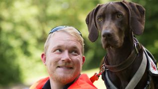Mann in Malteserkleidung schaut lächelnd zu einem großen braunen Hund mit Schlappohren auf
