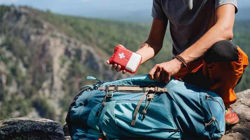 Ein Mann steckt auf einem Berg eine Erste-Hilfe-Tasche in seinen Rucksack.