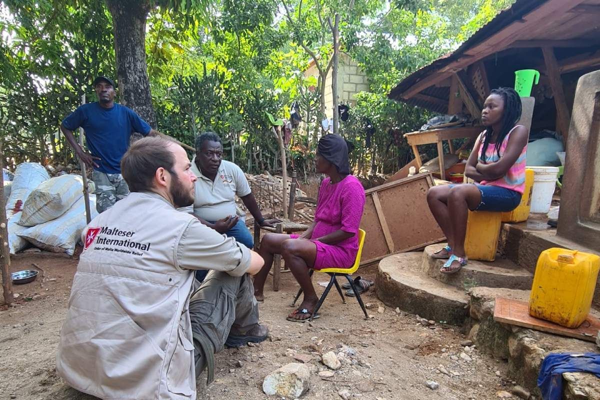 Fünf Menschen sitzen zwischen Trümmern und Müll in Haiti.