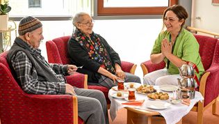 Eine Pflegekraft spricht am Kaffeetisch mit zwei älteren Menschen