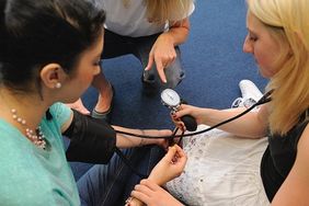 Menschen messen sich gegenseitig den Blutdruck mit einem Blutdruckmessgerät. Foto: Malteser