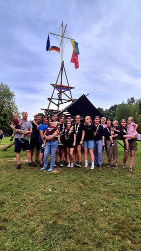 Gruppenfoto von zwanzig Jugendlichen und Gruppenleitungen der Malteser Jugend, die auf einer Wiese vor einem Bannermast stehen. Auf dem Banner steht Bunte Bande.
