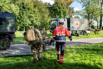 Zwei Soldaten der Bundeswehr und ein Helfer des Malteser Rettungsdienstes transportieren einen Soldaten auf einer Trage.