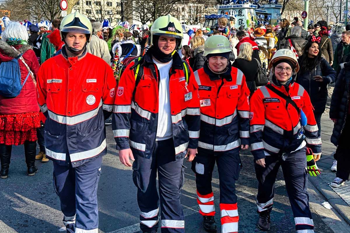 Drei Männer und eine Frau in Einsatzkleidung und Helm laufen auf einer asphaltierten Straße entlang. 