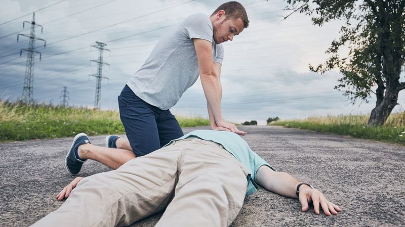 Junger Mann belebt einen anderen Mann auf einem asphaltierten Weg wieder.