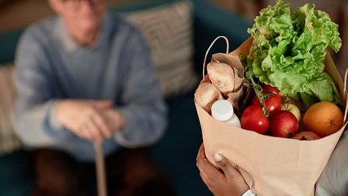 Ein alter Mann bekommt ein Papiertüte mit frischem Obst und Gemüse.