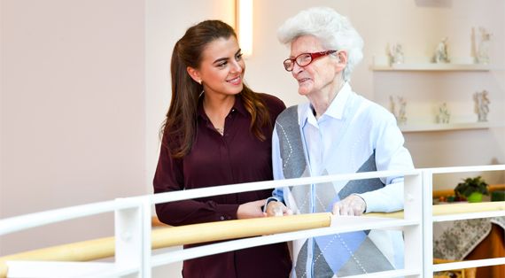 Pflegekraft geht mit Bewohnerin den Flur entlang