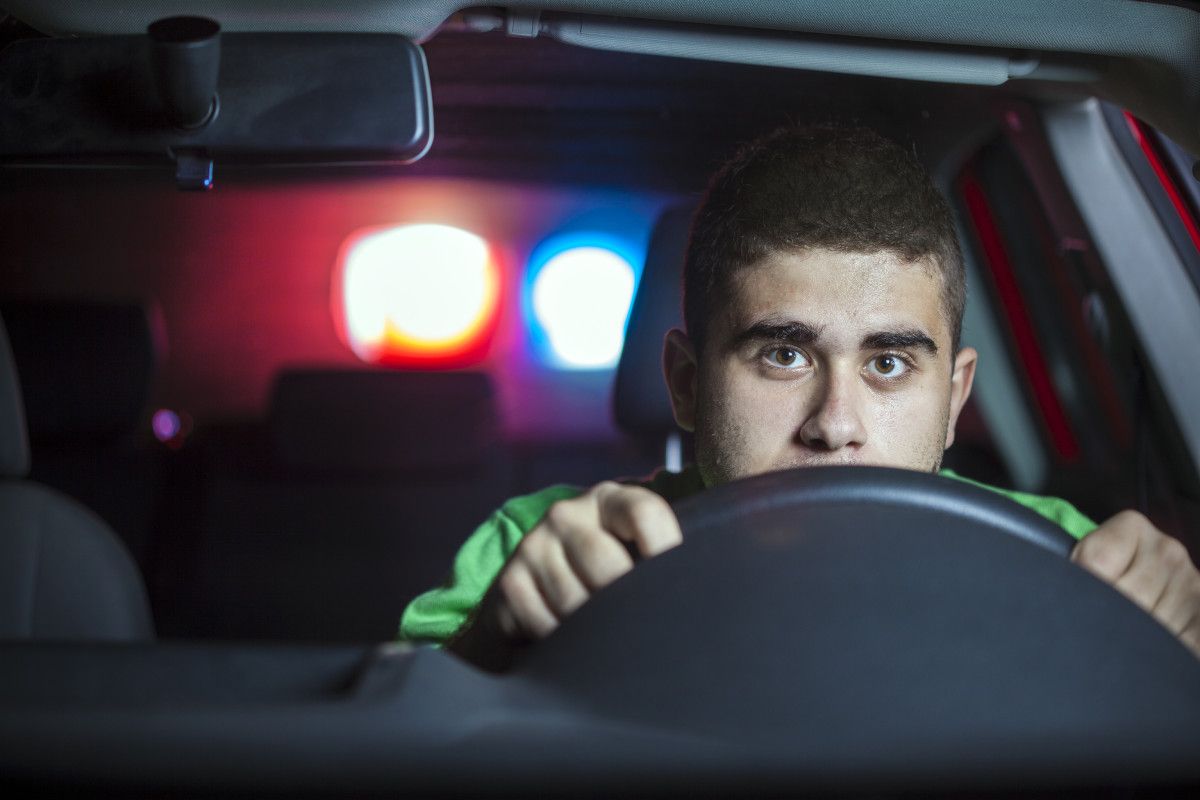 Junger Mann am Steuer eines Autos mit Blaulicht im Hintergrund.