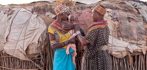 Zwei Frauen mit einem Baby stehen vor einer Hütte