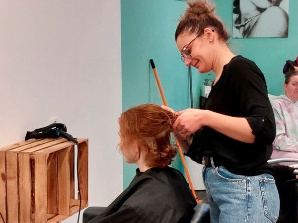 Eine lächelnde Friseurin schneidet die Haare einer Frau.