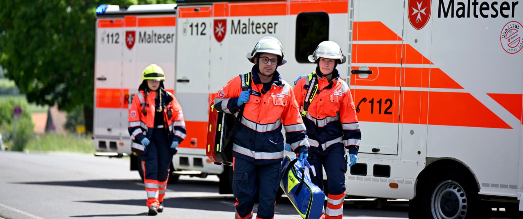 Drei Malteser Mitarbeitende vor Rettungswagen, bereit für den nächsten Einsatz.