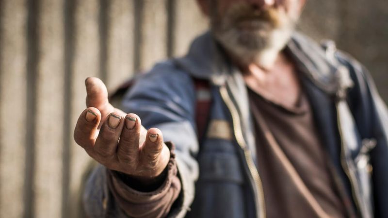 Obdachloser Mann streckt Hand aus.