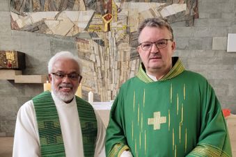 Zwei katholische Geistliche in grüner liturgischer Kleidung stehen in einer Kapelle vor einem Wandkreuz.