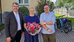 Ein Mann, eine Frau mit Blumenstrauß und ein weiterer Mann.