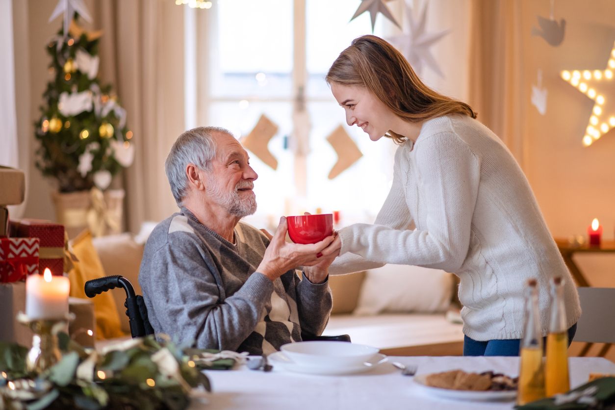 Eine junge Frau gibt einem älteren Mann im Rollstuhl einen Tasse Tee.