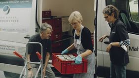 Zwei Frauen und ein Mann laden Lebensmittel aus einem Transporter aus.