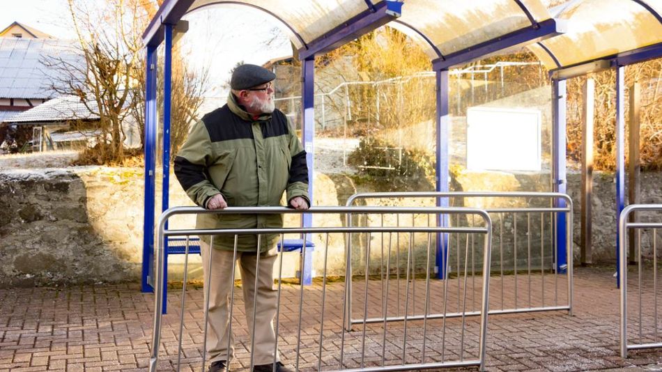 Ein alter Mann an einer Bushaltestelle.
