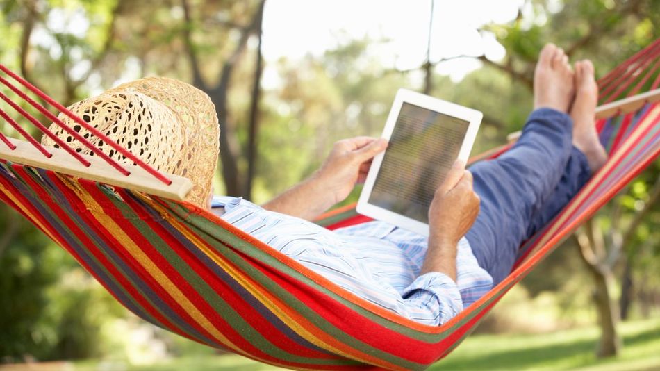 Eine ältere Frau liegt in der Hängematte und liest ein E-Book.
