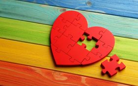 Rotes Herzpuzzle mit zwei fehlenden Teilen auf einem Hintergrund mit Regenbogenfarben.