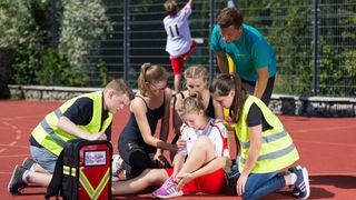 Malteser Schulsanitäter versorgen ein Mädchen, das sich beim Sport verletzt hat.