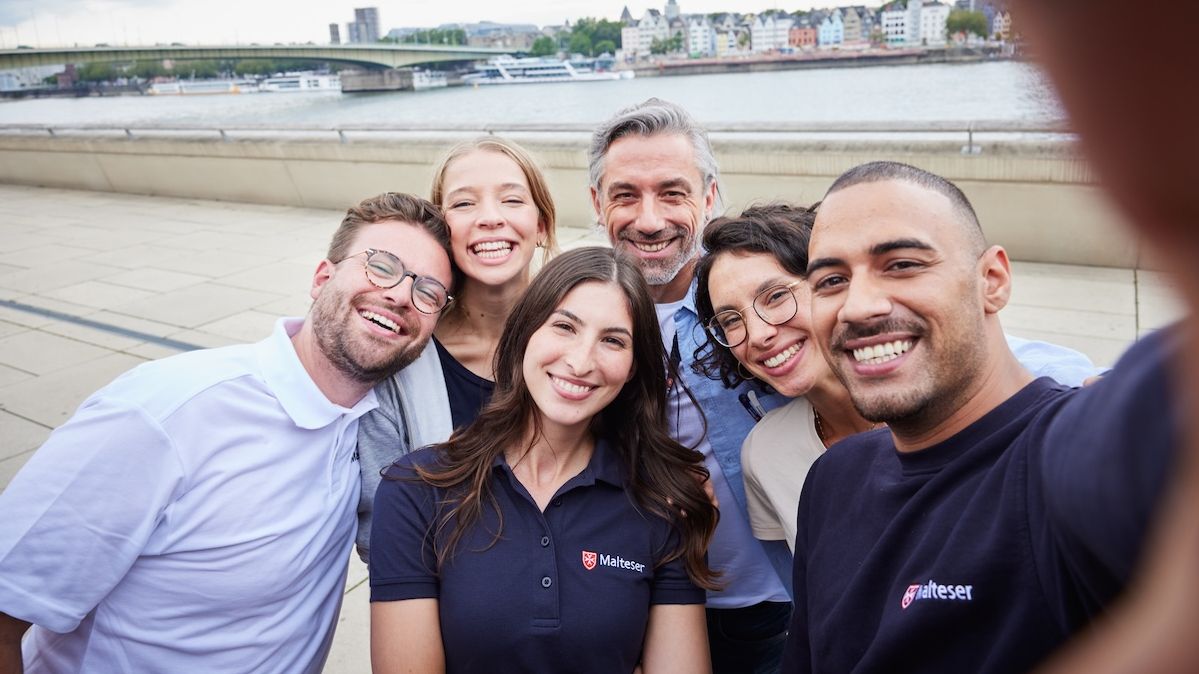 Sechs Mitarbeitende der Malteser stehen an einem Flussufer und nehmen ein Selfie auf.