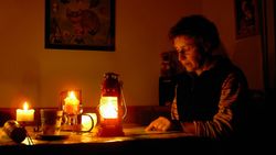 Eine Frau sitzt bei Kerzenschein und Laternen an einem Tisch und liest