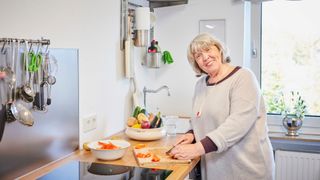 Seniorin trägt einen Hausnotruf Notfallknopf als Notrufkette und kocht.