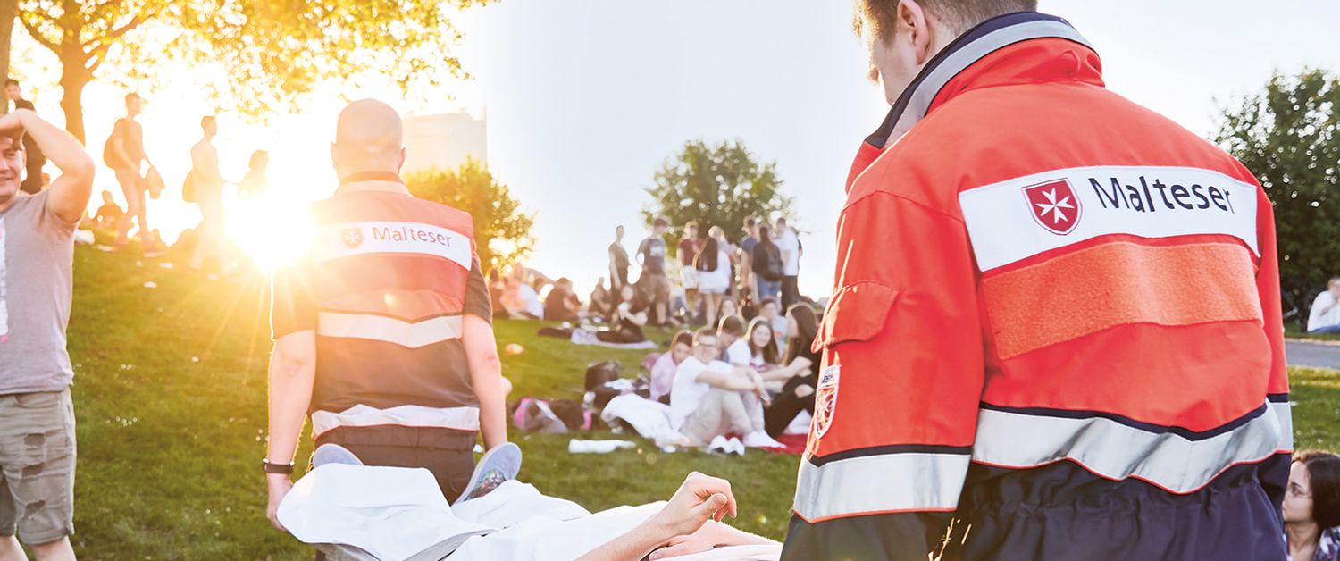 Malteser Einsatzsanitäter tragen einen Verletzten über ein Festivalgelände.