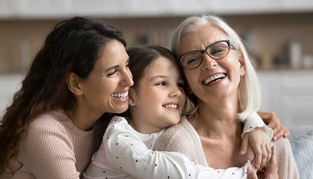 Eine Seniorin, eine Frau und ein Mädchen umarmen sich lachend