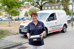 Mitarbeiterin des Malteser Menueservice trägt eine Warmhaltebox und lächelt in die Kamera.