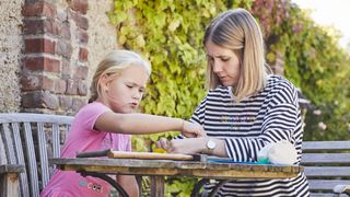 Eine Malteser Helferin sitzt mit einem Mädchen am Tisch und spielt.
