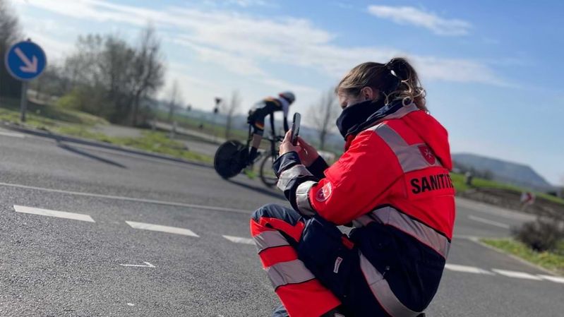  Eine Angehörige des Malteser Sanitätsdienstes filmt Rennradfahrer mit einem Smartphone.