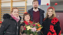 Eine Frau hält einen Blumenstrauß. Um sie herum stehen Menschen, die ihr gratulieren. 