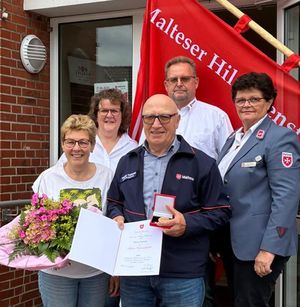 Fünf Personen in Malteser-Dienstbekleidung. Die vorne stehende Person hält eine Urkunde in der Hand.
