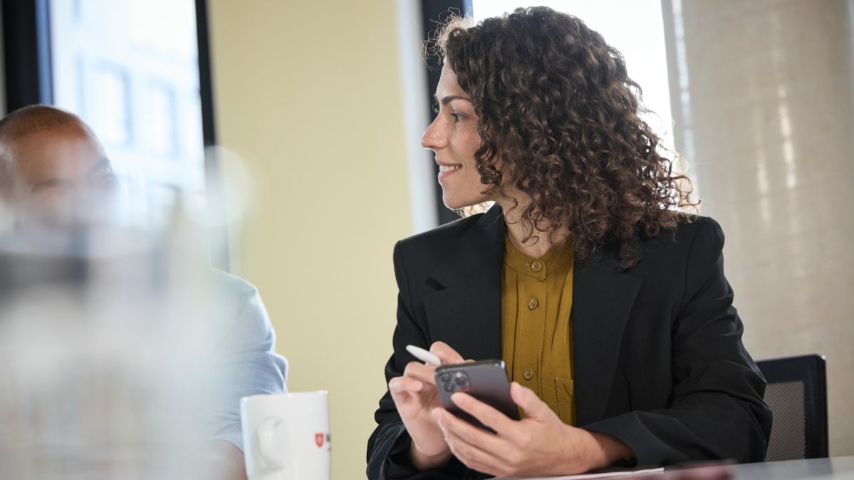 Trainee der Malteser sitzt mit einem Smartphone in der Hand in einer Besprechung