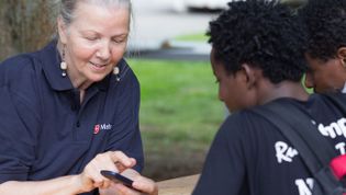 Eine Mitarbeiterin der Malteser Flüchtlingsbetreuung zeigt zwei Jungen etwas auf dem Handy.