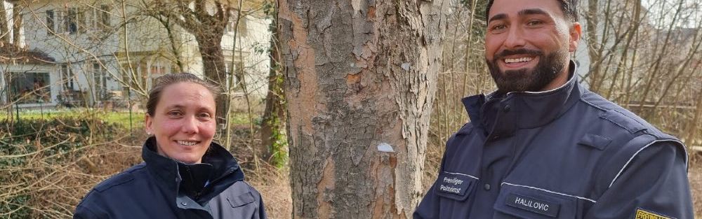 Ein Mann und eine Frau in Uniformen des Freiwilligen Polizeidienstes lächeln in die Kamera.