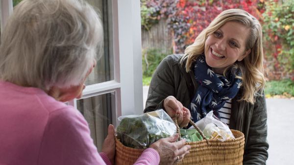 Junge Frau übergibt einer älteren Frau einen Einkaufskorb.