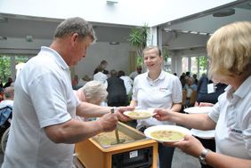 Männer und Frauen teilen Erbseneintopf an Wallfahrende aus.