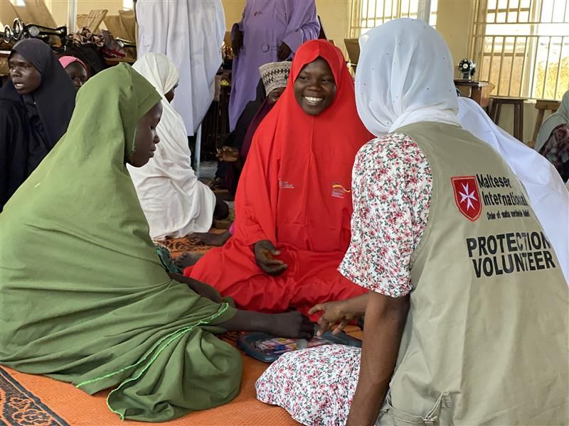 Drei Frauen sitzen im Kreis auf dem Boden und lächeln