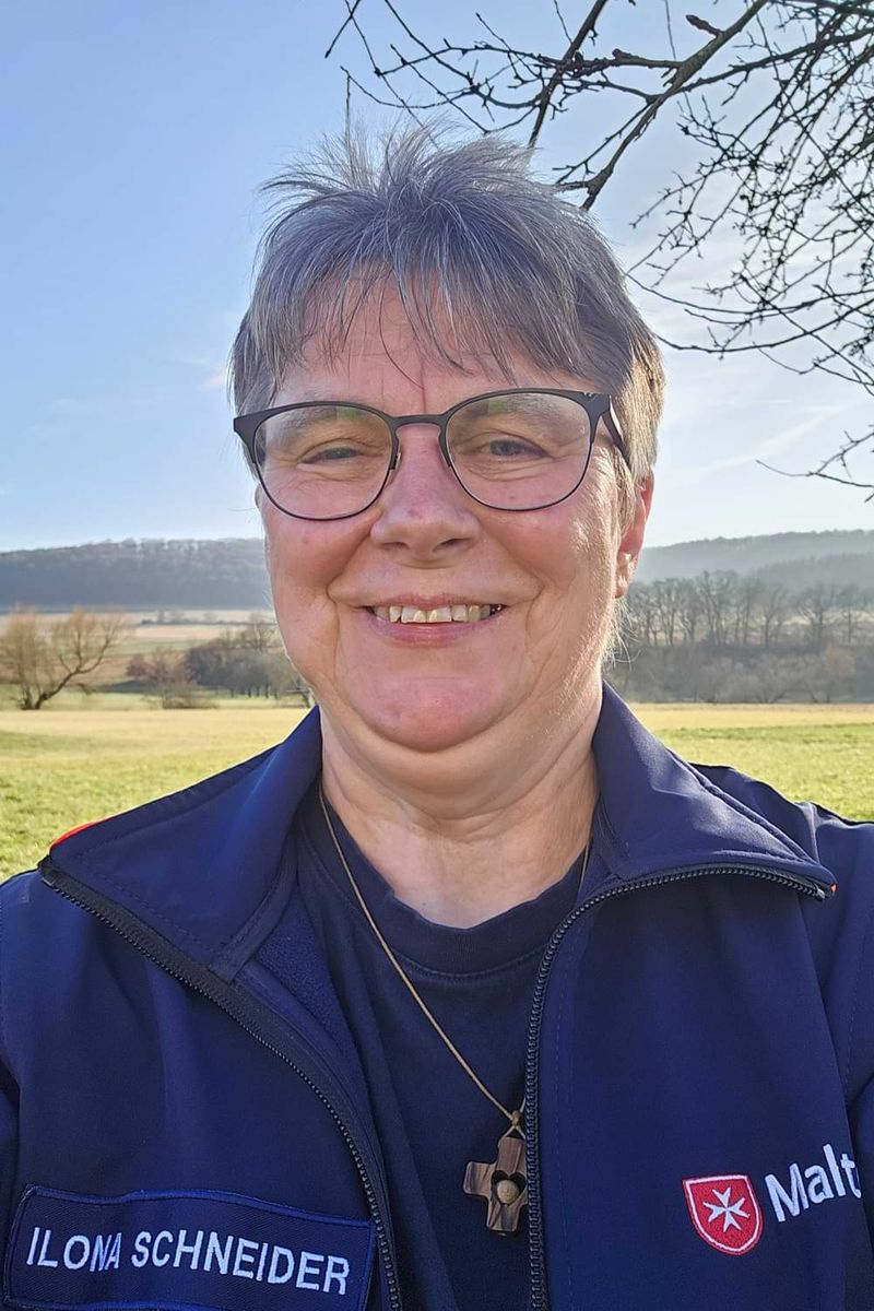 Selfie einer lächelnden Frau mit Brille auf einem Feld. 