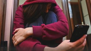 Eine Person sitzt zusammengekauert in einer Tür und hält ein Smartphone in der Hand.