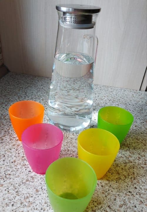 Wasserkaraffe mit bunten Bechern. 